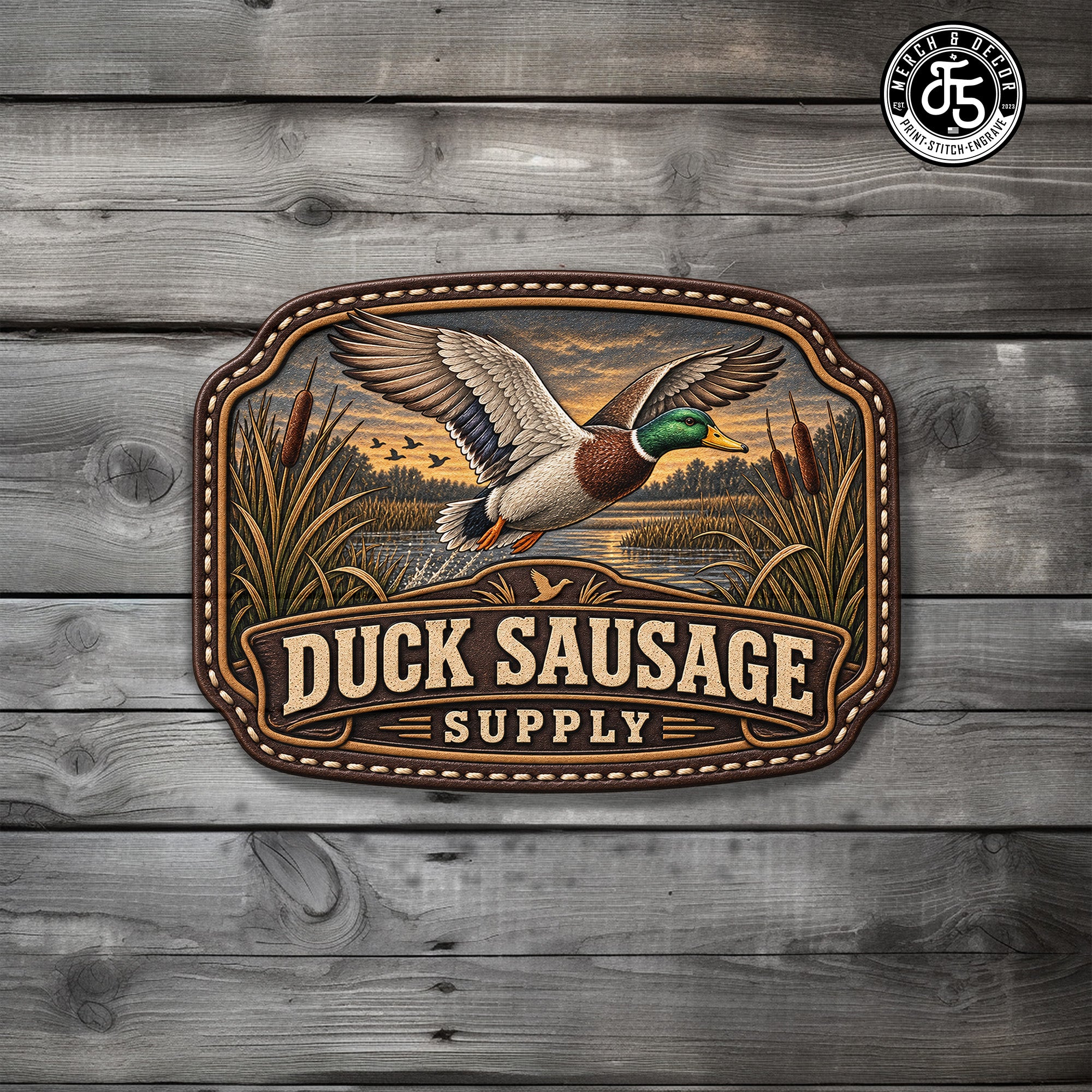A decorative rectangular UV Printed Patch with rounded corners featuring an illustration of a mallard duck flying over a marsh at sunset, with the text 'DUCK SAUSAGE SUPPLY' across the bottom. The hat patch is displayed against a gray wood plank background.