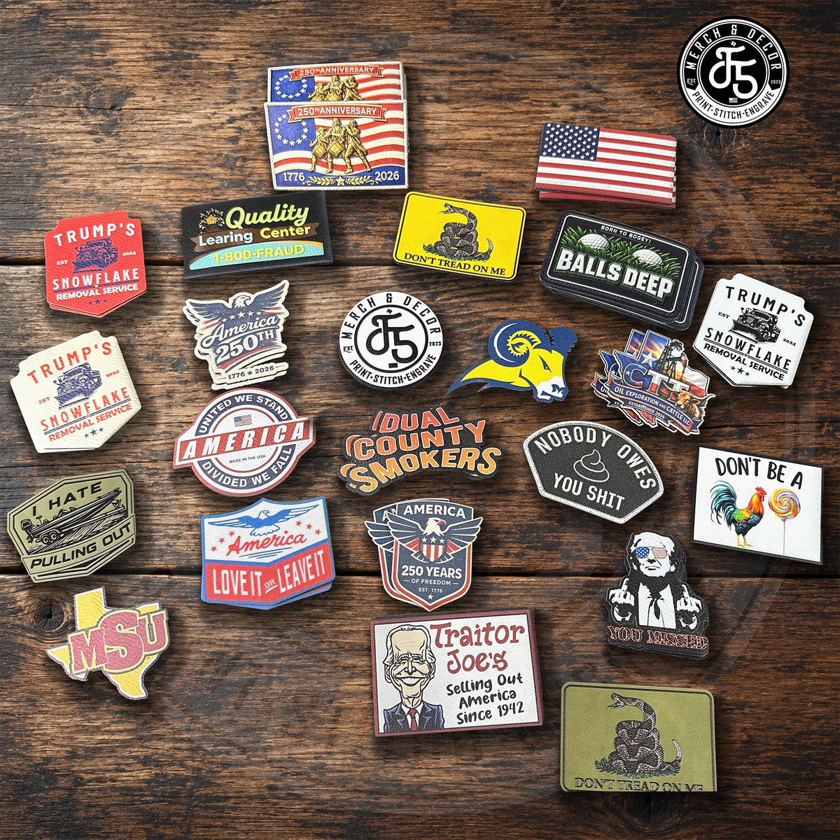 A collection of 20 distinct UV Printed Hat Patches arranged on a dark wooden background. The Custom UV Printed Hat patches feature various political, historical, and cultural slogans, including Trump, NSU, Texas, and the Gadsden flag design.