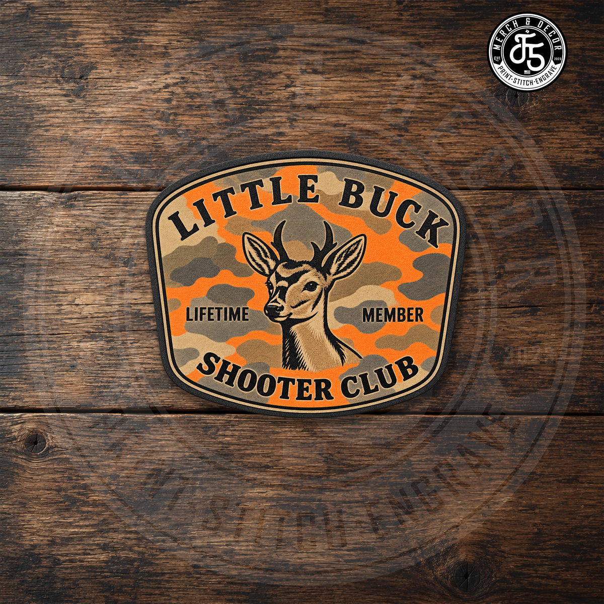 Little Buck Shooter Blaze Camo UV printed hat patch displayed on dark rustic wood