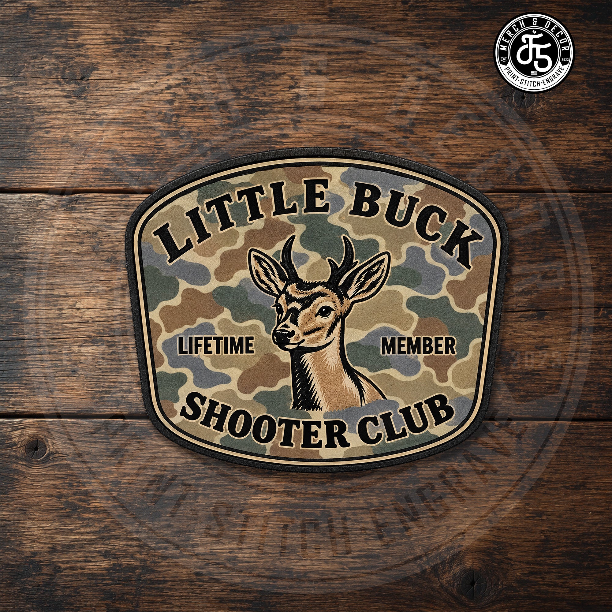 Little Buck Shooter Backwoods Camo UV printed hat patch displayed on dark rustic wood